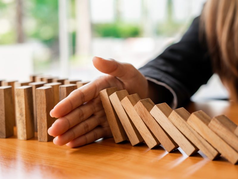 A businesswoman blocks a falling wooden block like a domino. It is like stopping business risks with