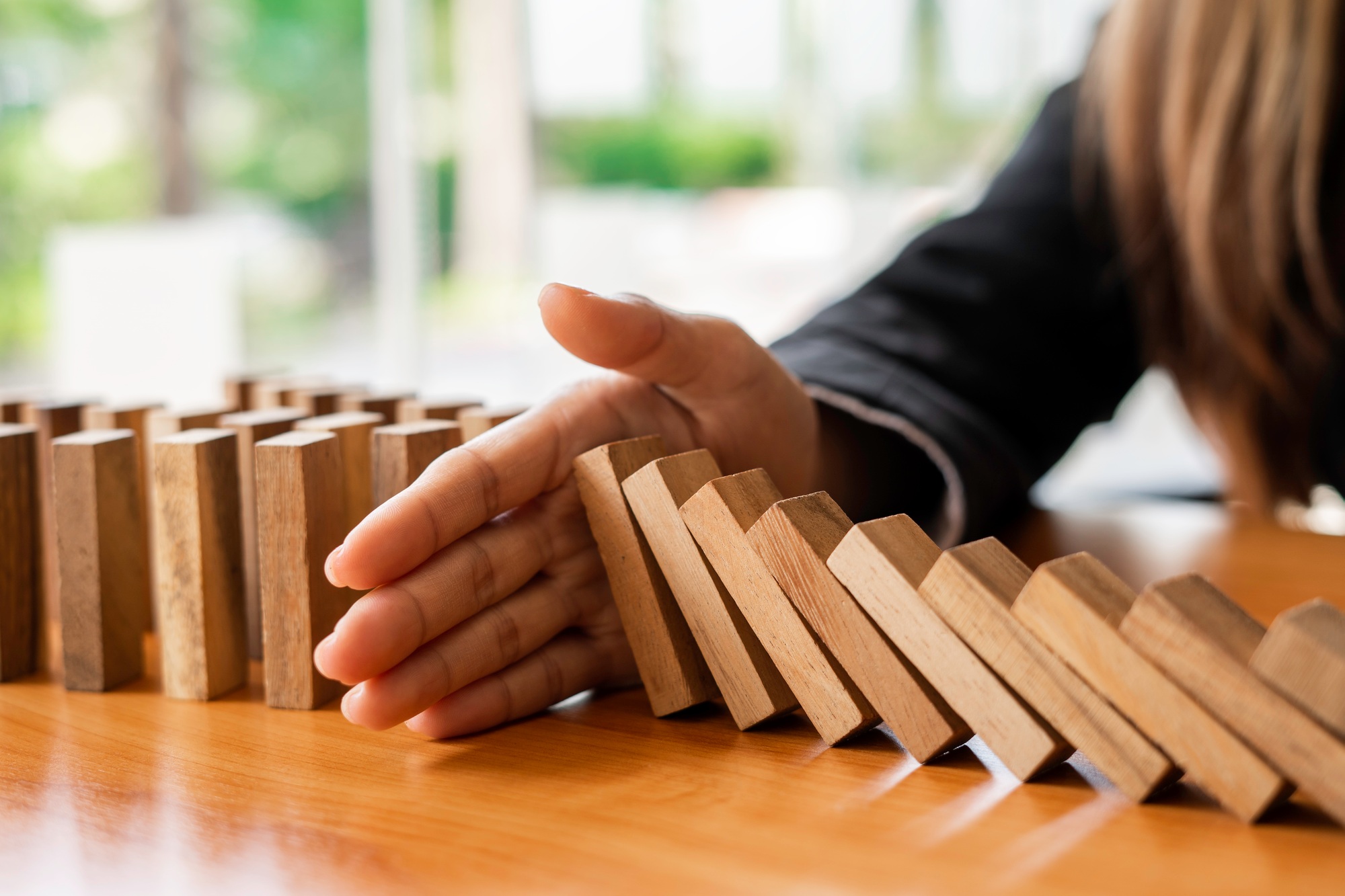 A businesswoman blocks a falling wooden block like a domino. It is like stopping business risks with